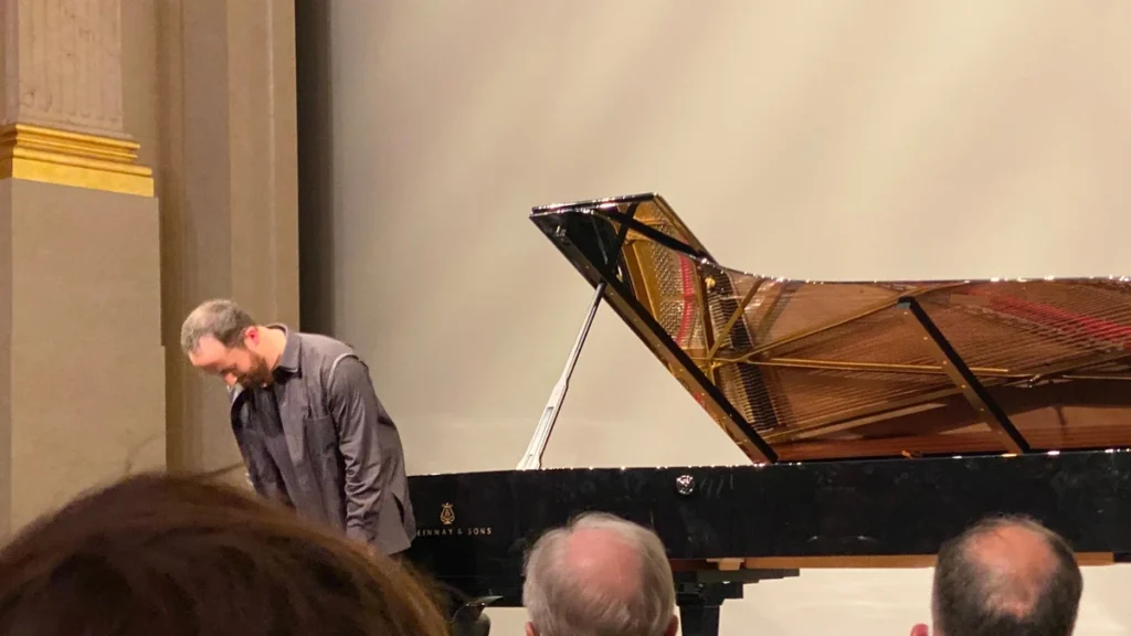 Igor Levit taking applause beside a concert grand piano