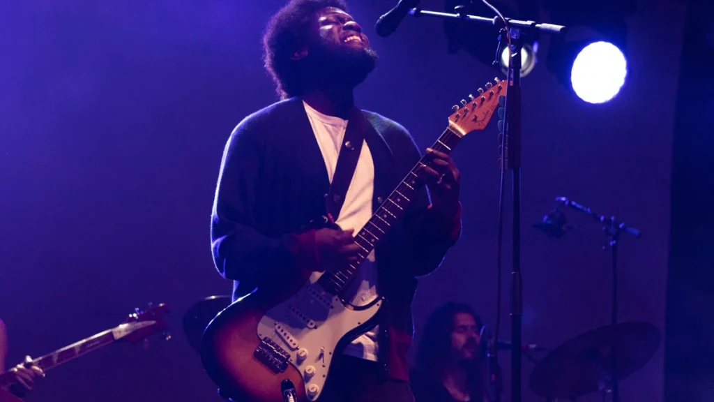 Michael Kiwanuka performing live with a Fender guitar under purple stage lighting