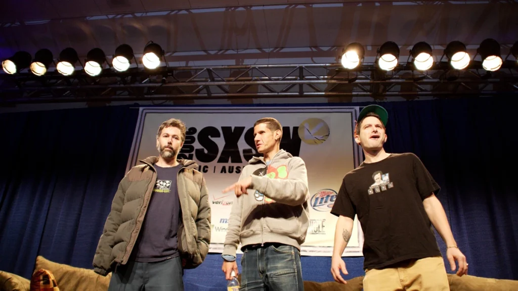 The three members of the Beastie Boys standing on a stage under lights
